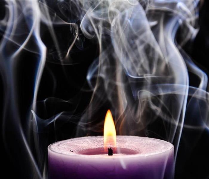 Purple candle with smoke all around it with a black background.