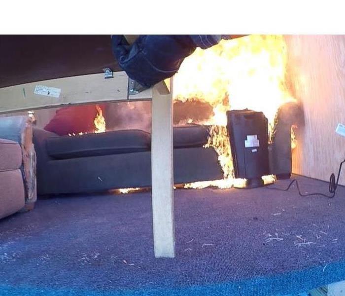 Space heater on fire in a living room next to a couch.