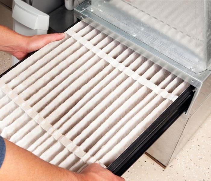 A person replacing a furnace filter in a furnace.